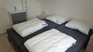 A double bed with white bedding, a bedside table with a lamp, and a small shelf unit. - House in Breskens Near Beach and Lighthouse (Breskens)