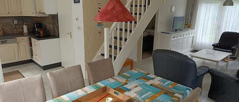 A dining area with a wooden table, chairs, a red pendant light, and a staircase leading to another level.