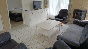 A living room with a sofa, a coffee table, a TV on a cabinet, a chair, and a fireplace. - House in Breskens Near Beach and Lighthouse (Breskens)