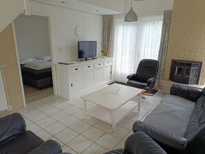 A living room with a sofa, a coffee table, a TV on a cabinet, a chair, and a fireplace. - House in Breskens Near Beach and Lighthouse (Breskens)