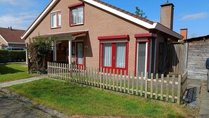 A two-story brick house with a red and white facade, a wooden fence, and a clear sky. - House in Breskens Near Beach and Lighthouse (Breskens)