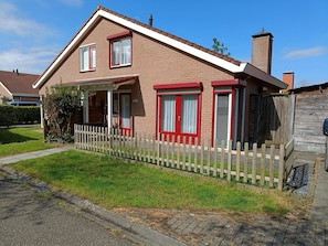 A two-story brick house with a red and white facade, a wooden fence, and a clear sky. - House in Breskens Near Beach and Lighthouse (Breskens)
