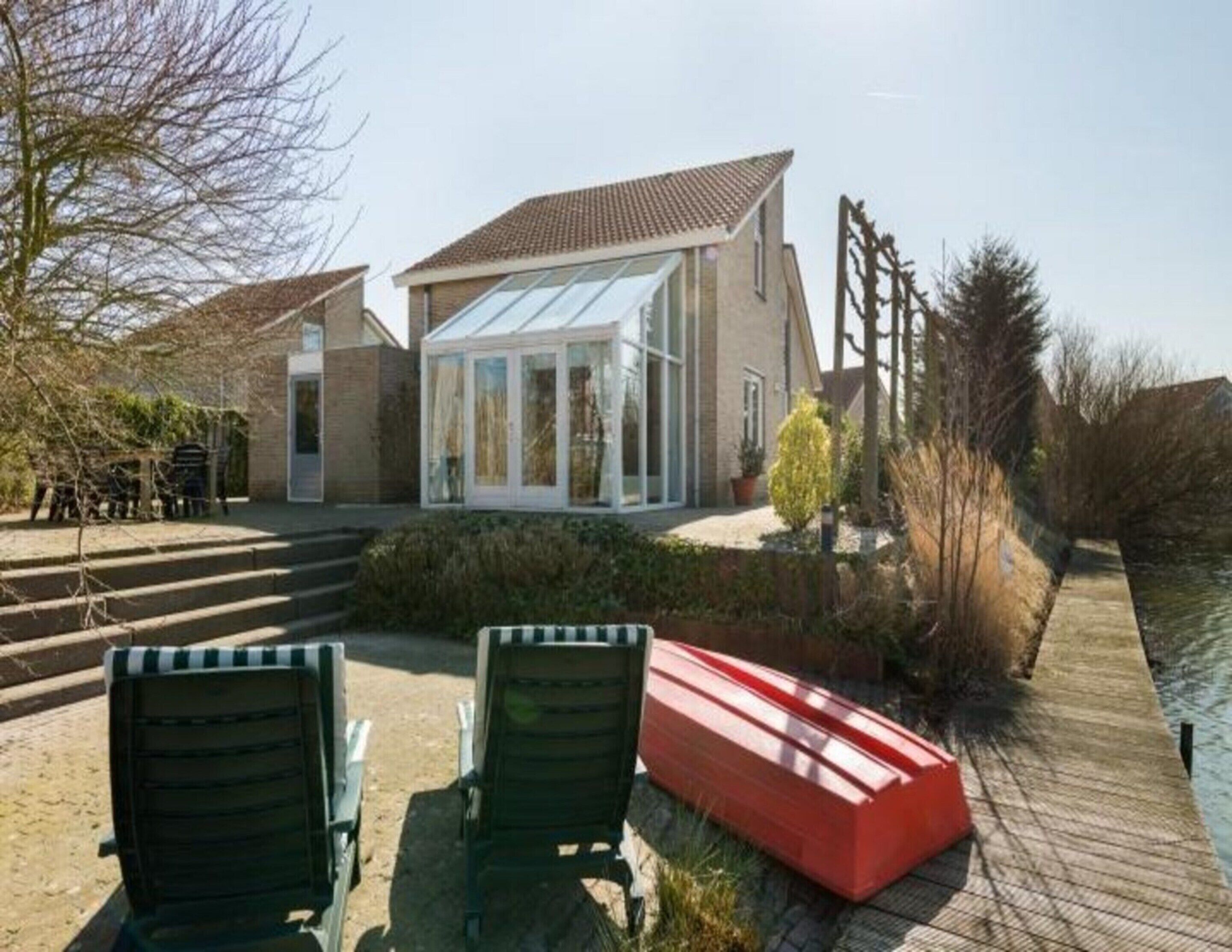 A modern house with a glass conservatory, a wooden deck, and a red boat.