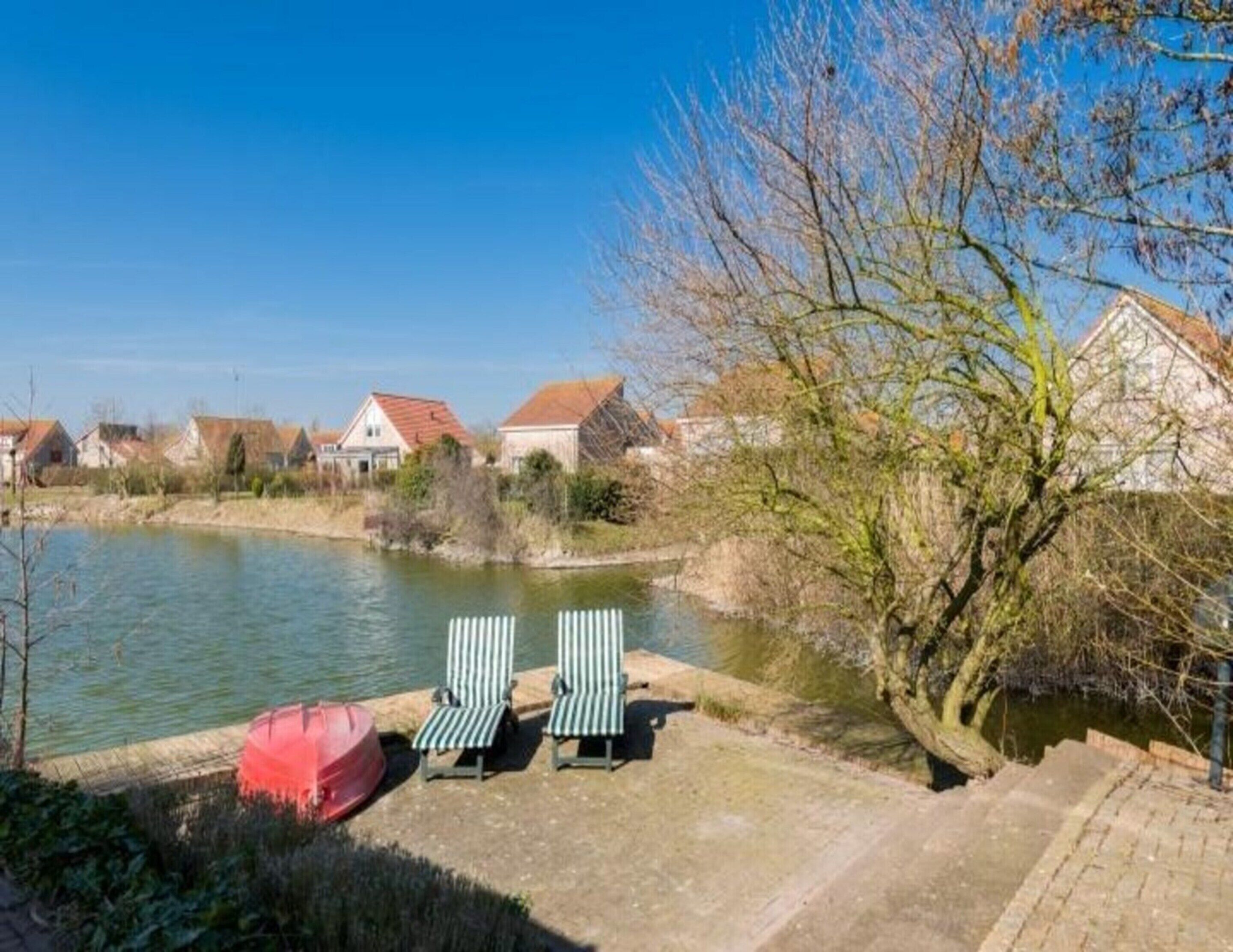 A riverside view with a row of houses, a tree, and two striped lounge chairs by the water.