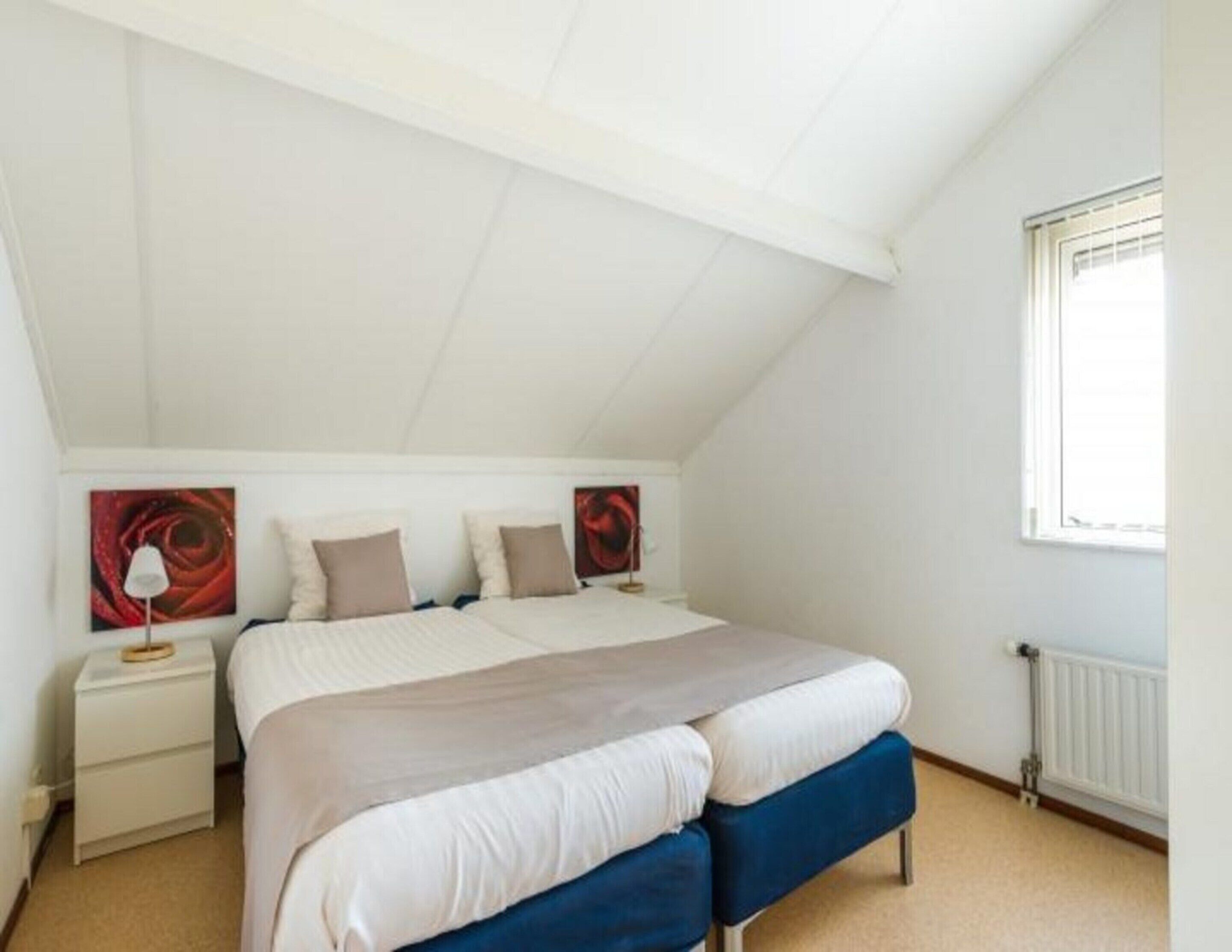 A bedroom with a sloped ceiling, a bed with a blue bench, white bedding, and two bedside tables with lamps.