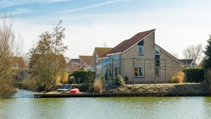 Een huis aan een rustige rivier met een steiger en stoelen.