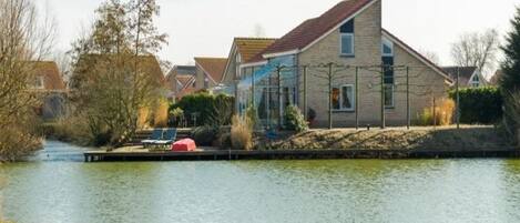 A house by a calm river with a dock and chairs.