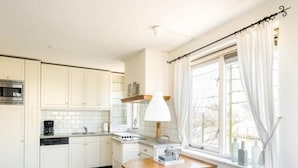 Een keuken met witte kasten, een fornuis, een spoelbak en een raam met gordijnen.