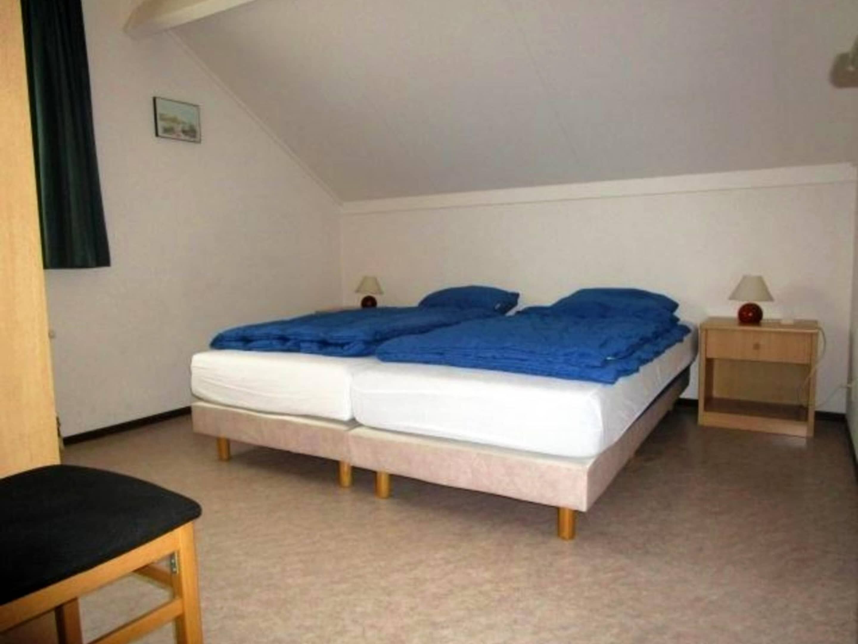Ein Zimmer mit einem Bett, zwei Nachttischen, einem Sessel und einem Bild an der Wand.