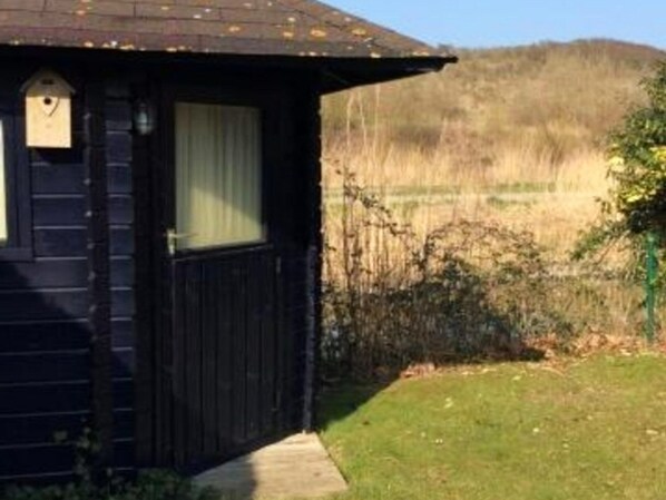 A small wooden cabin with a window and a door, surrounded by a grassy area and a fence.