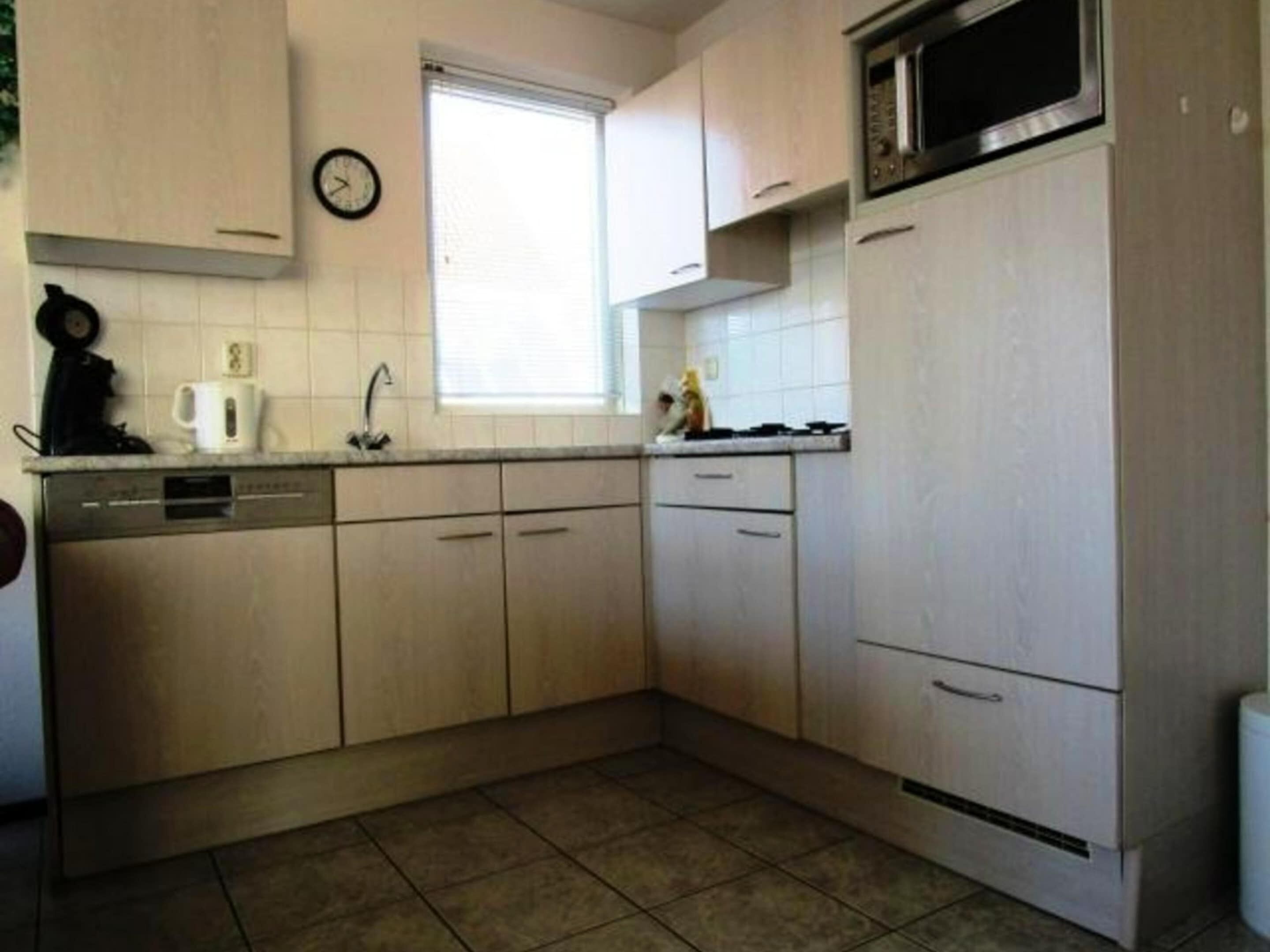 A kitchen with light-colored cabinets, a microwave, a clock, and a window.