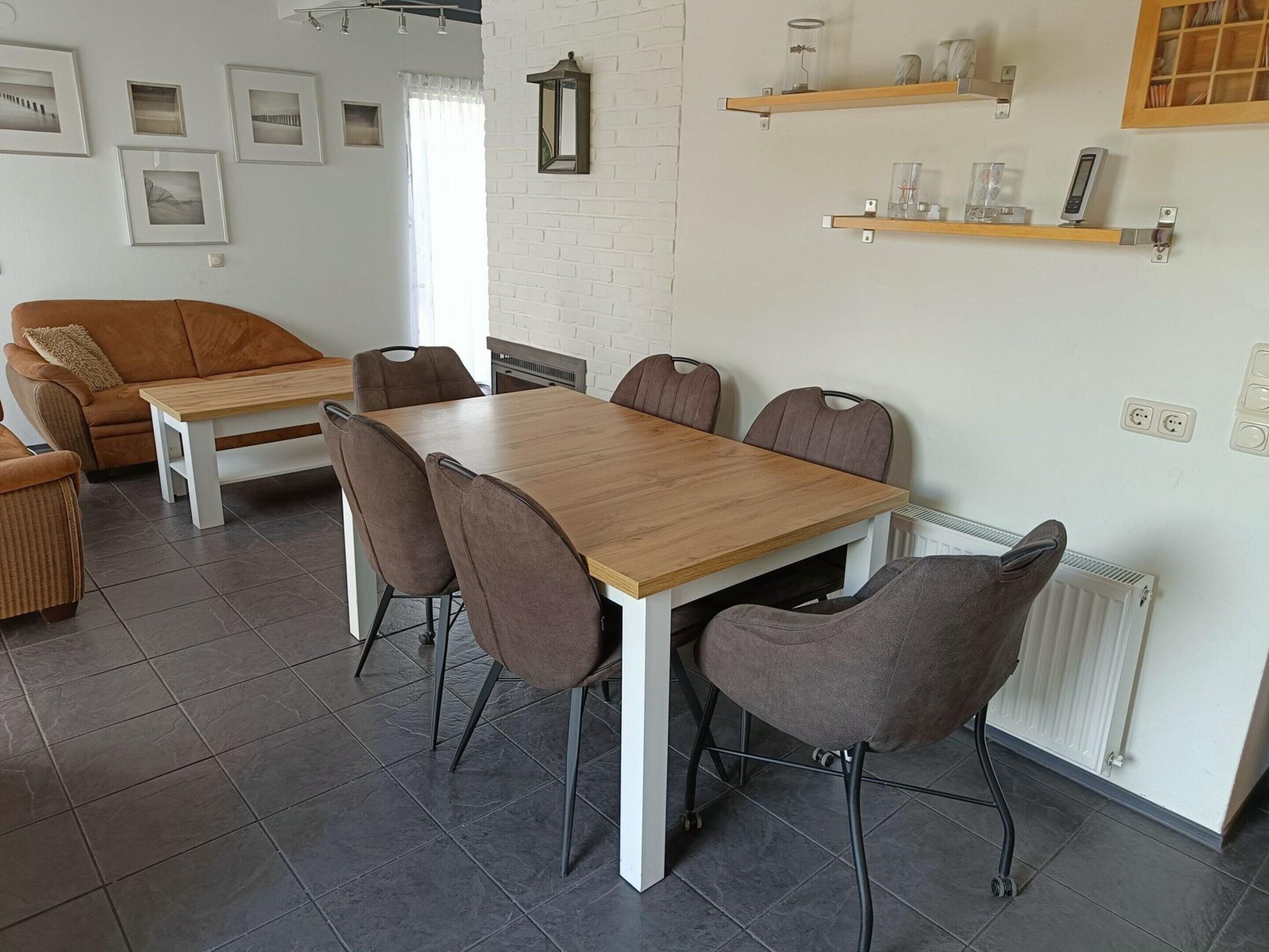 A dining area with a wooden table and six chairs, a white brick wall, and a window with curtains.