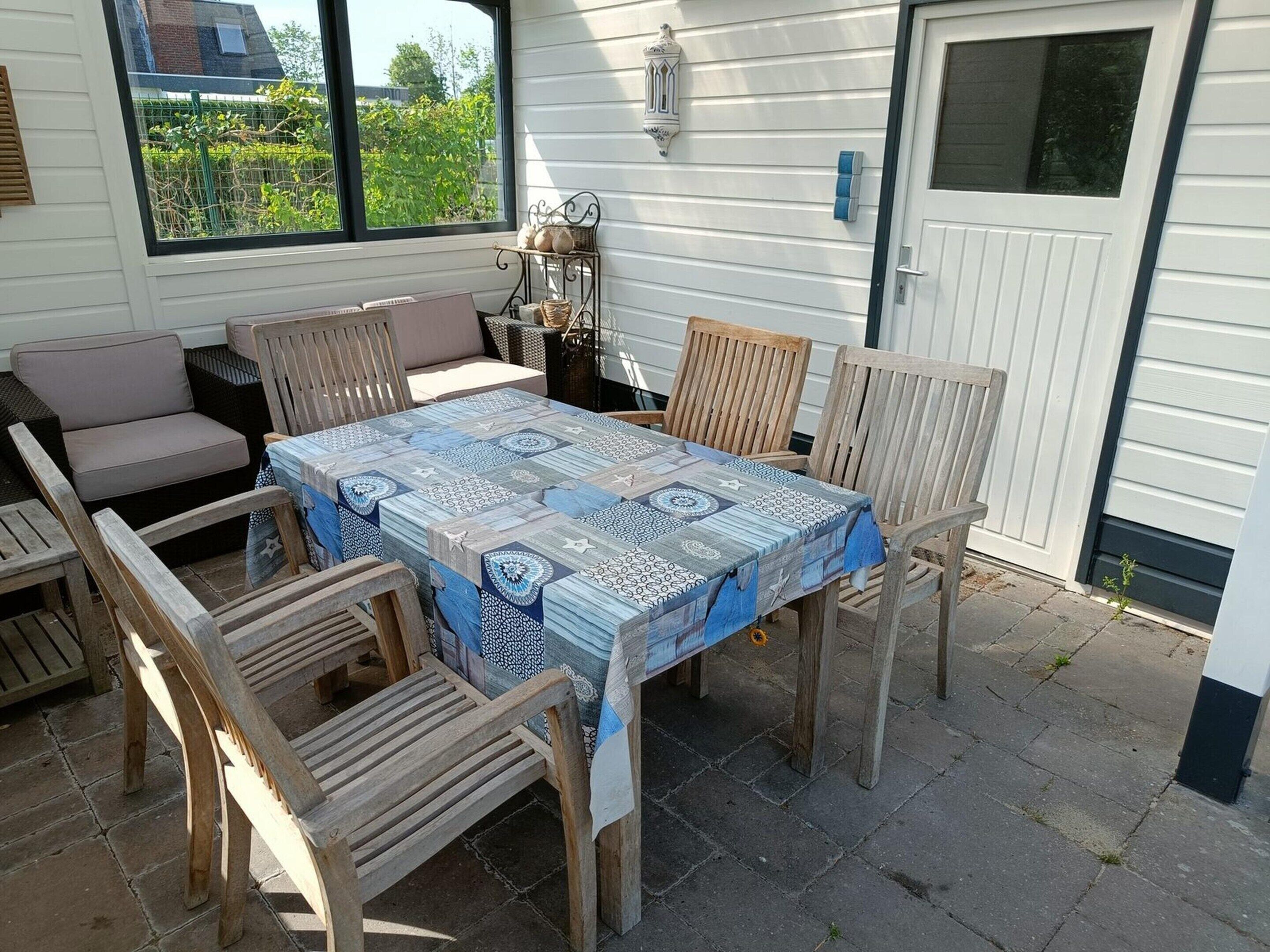 Een terras buiten met een tafel, stoelen, een rieten bank en een decoratieve lantaarn.