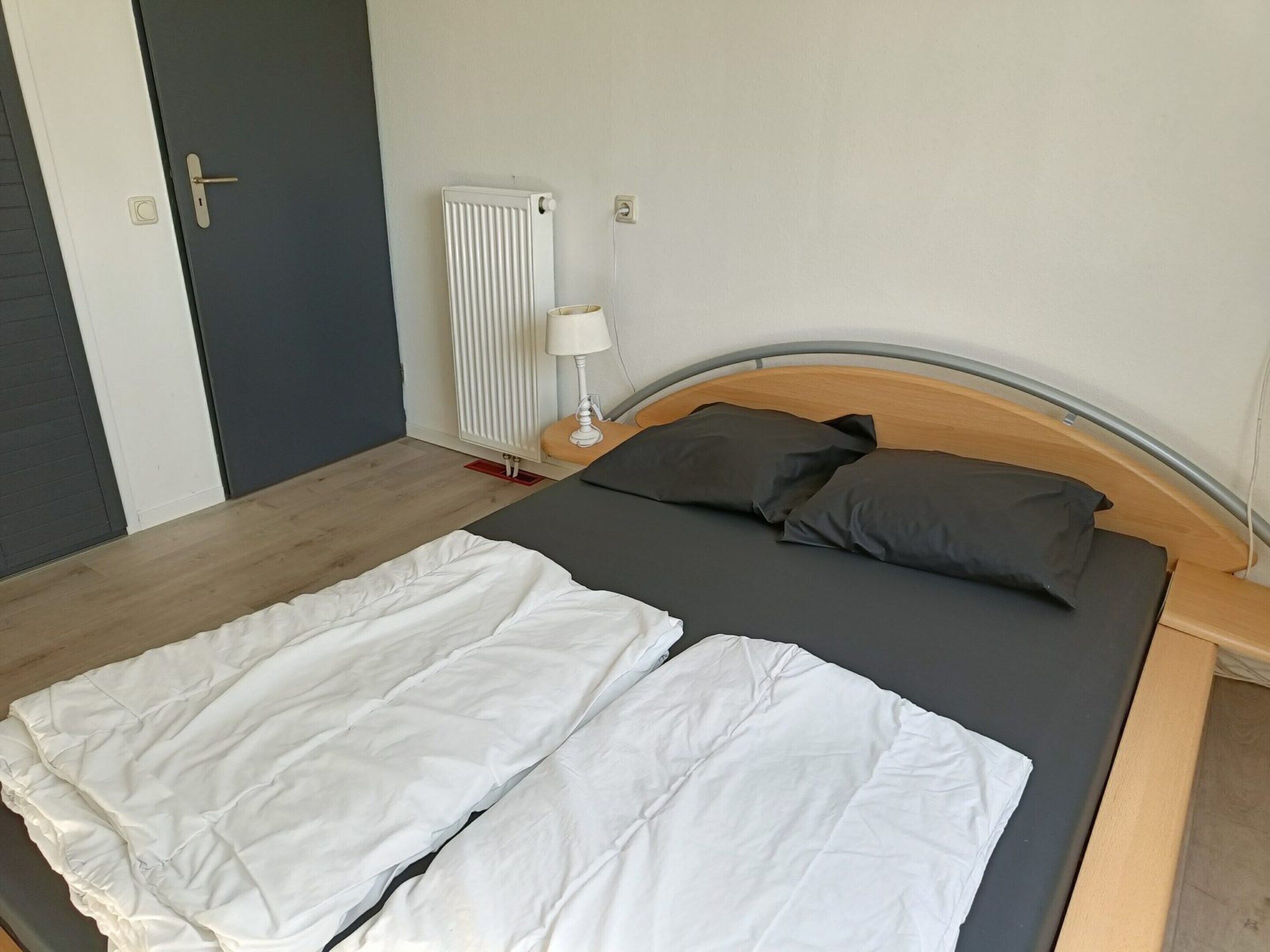 Un lit simple avec une tête de lit en bois, une couverture blanche et deux oreillers.