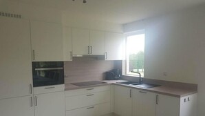 A kitchen with white cabinets, a built-in oven, a sink, and a window with a view of greenery. - Coastal Bungalow w/ Garden (Breskens)