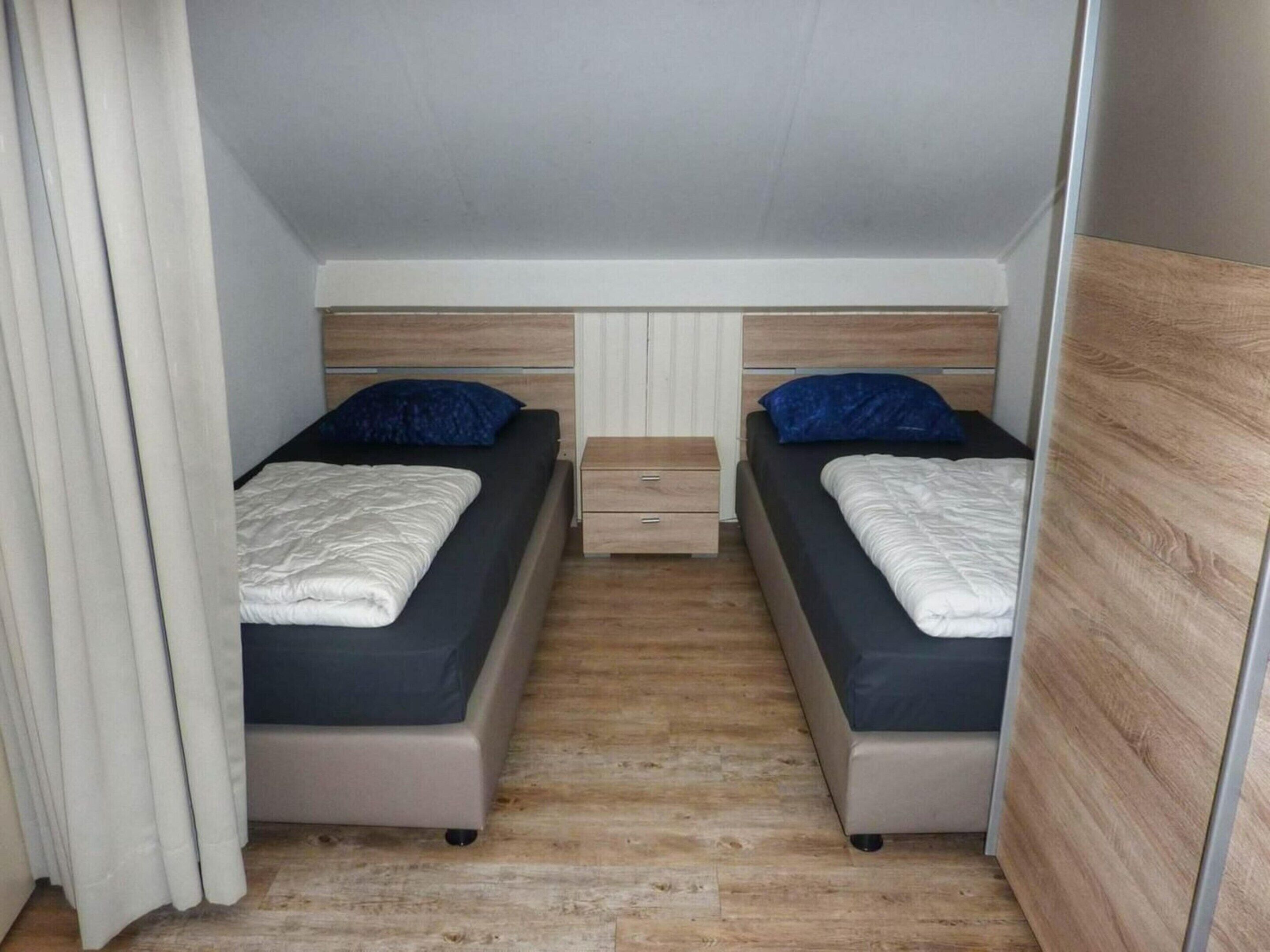 Une chambre de taille modeste, comprenant deux lits, une petite table de chevet et une armoire.