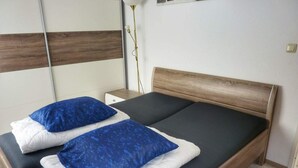 A double bed with a wooden headboard, two pillows, a bedside table, and a floor lamp. - Coastal Bungalow w/ Garden (Breskens)