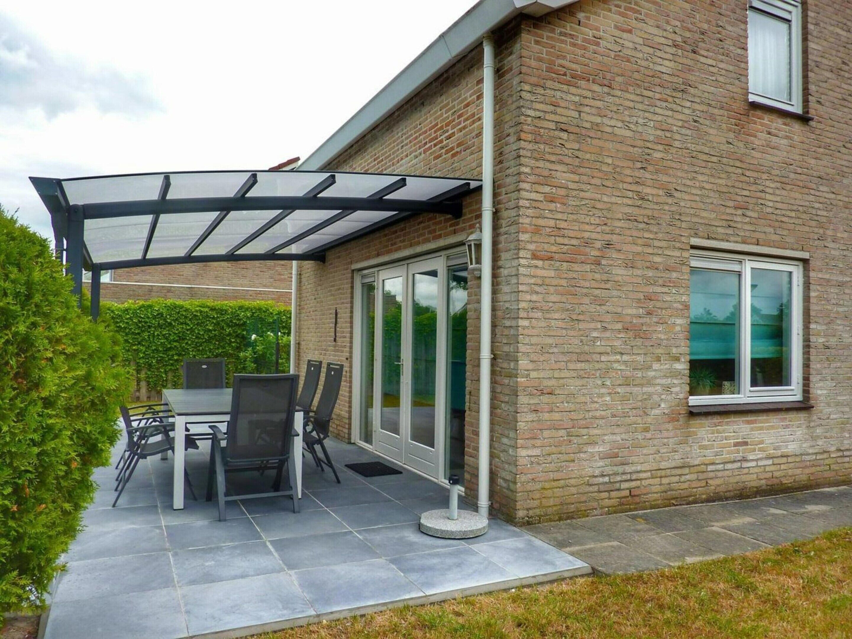 A patio with a glass enclosure, a table with chairs, and a brick house.