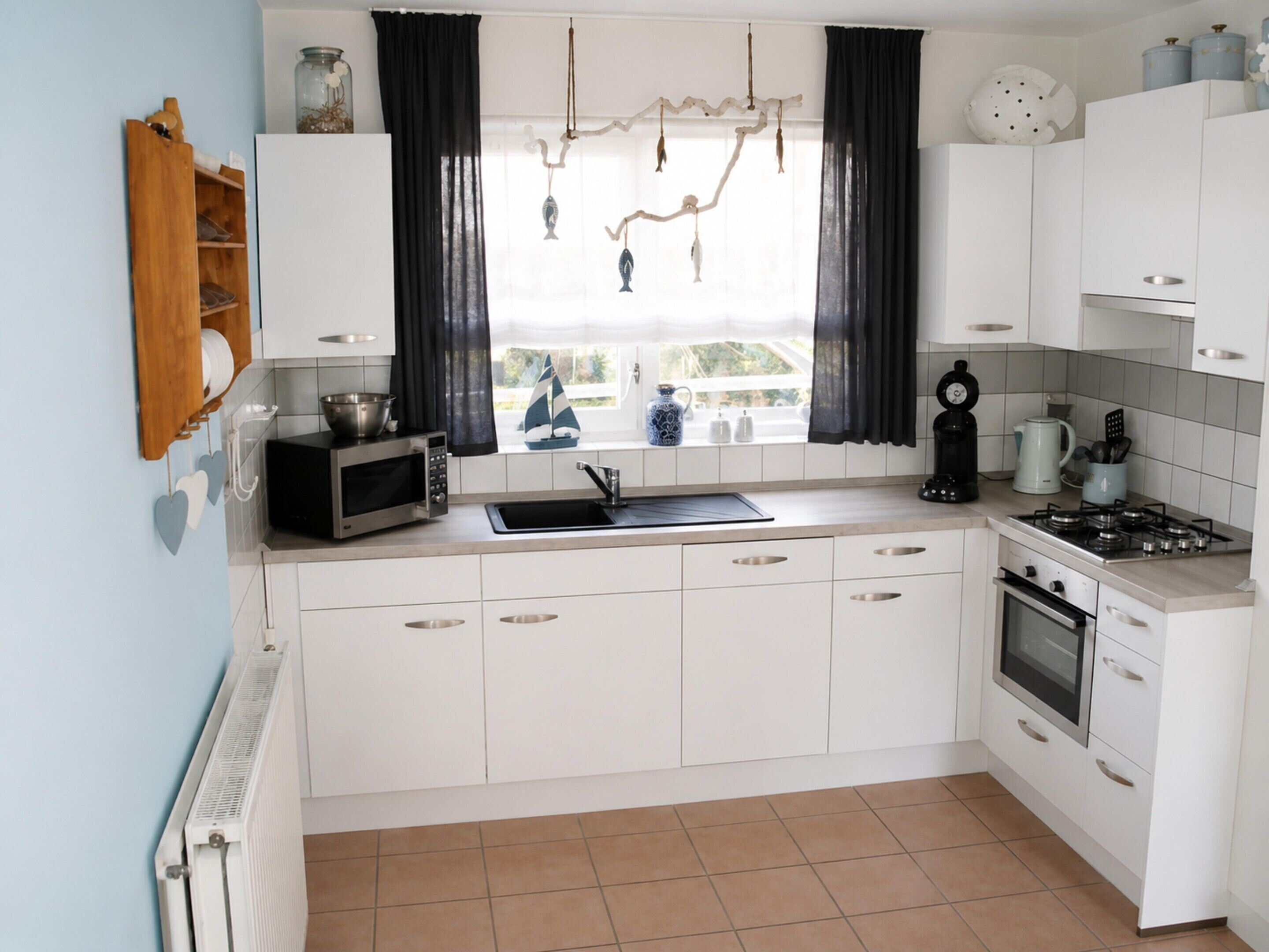 A kitchen with white cabinets, a stove, a microwave, a sink, and a window with curtains.