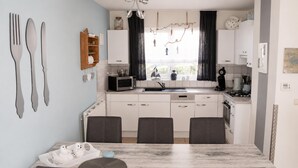 A modern kitchen with white cabinets, a microwave, and a sink. There is a dining table with four chairs. - Bungalow in Breskens Near the Beach (Breskens)