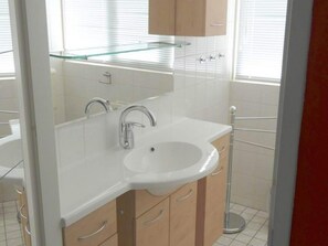 A bathroom with a white sink, two faucets, a glass shelf above the sink, and wooden cabinets. - Bungalow in Breskens Near the Lighthouse (Breskens)