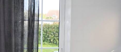 A room with a white door, a view of greenery outside, and a window with a curtain.
