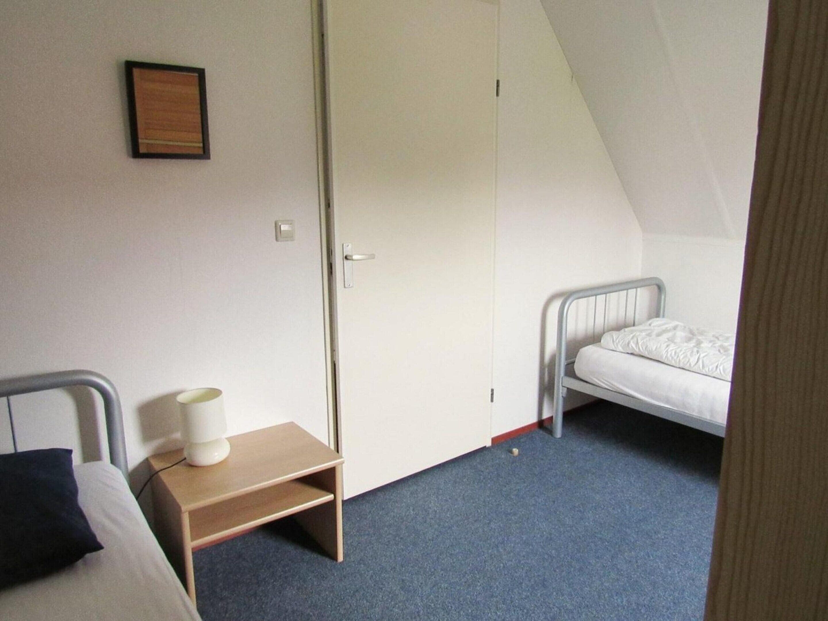 Un dormitorio con una cama individual, una mesita de noche con lámpara, un armario y un cuadro en la pared.