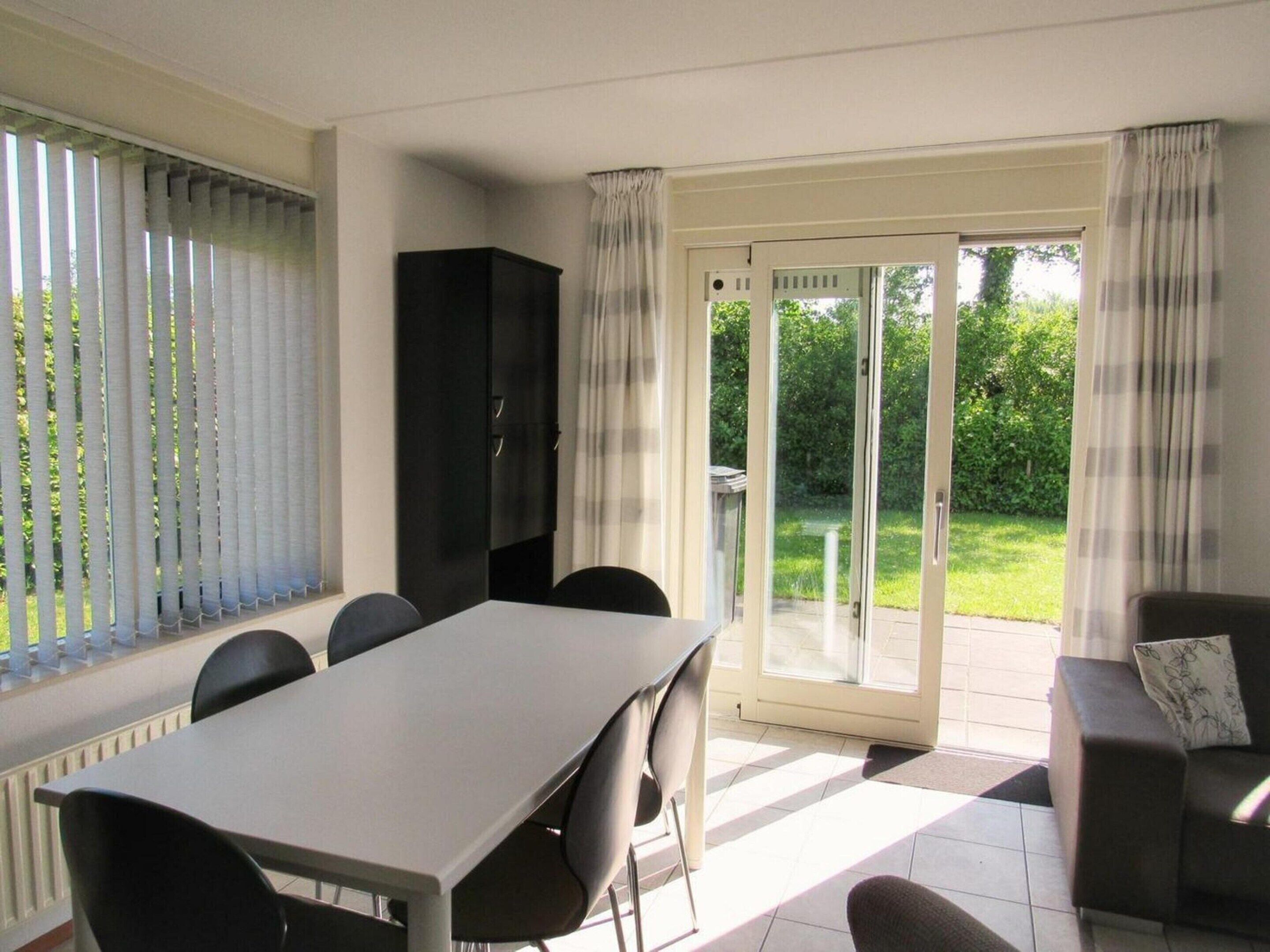 A dining area with a table and chairs, a black cabinet, and a sliding glass door leading to a garden.