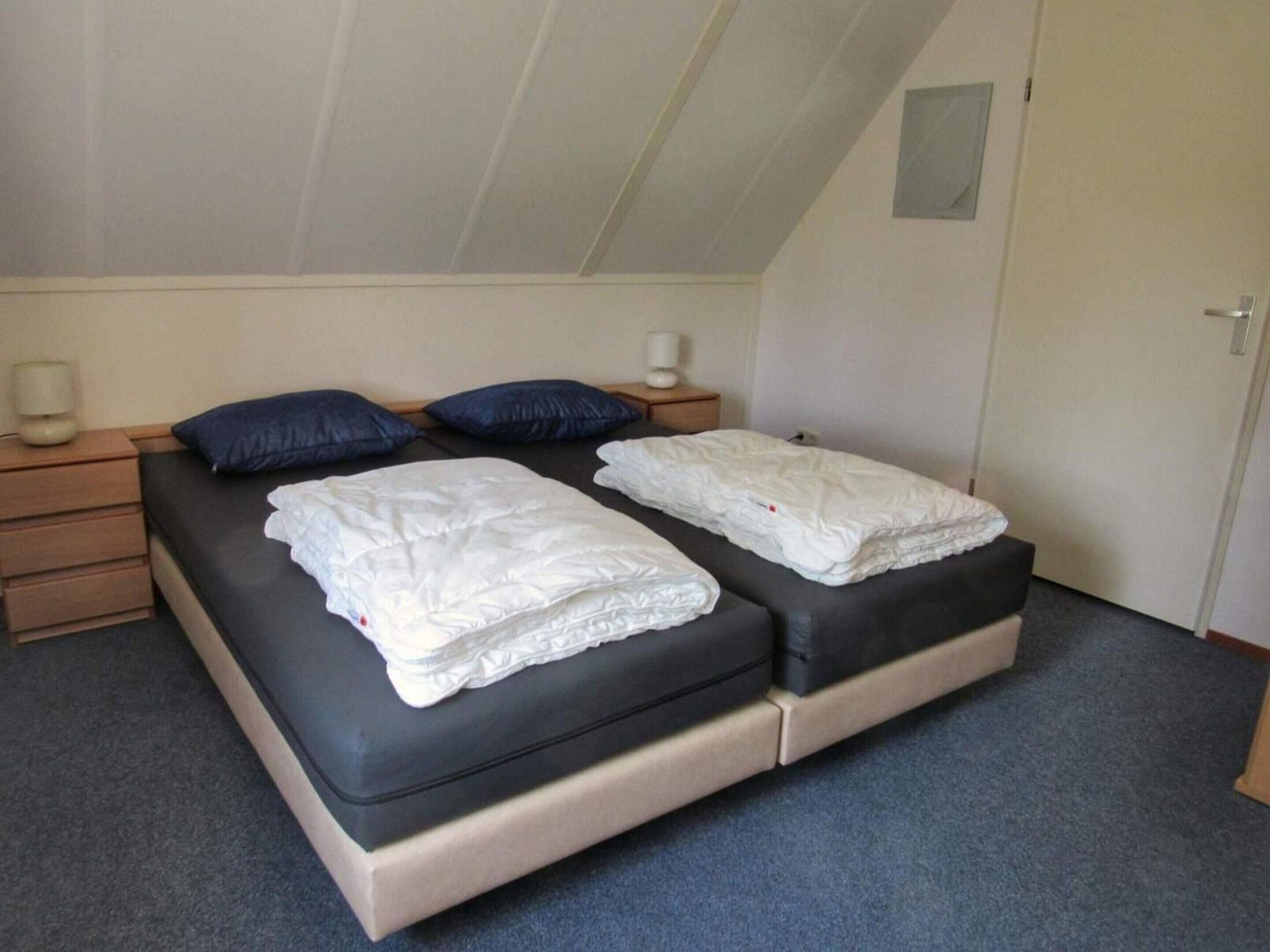 A room with a bed, two bedside tables, a nightstand, a lamp, and a door.