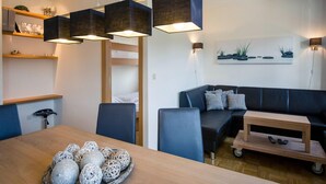 A modern living room with a sofa, a dining table with decorative items, and a bunk bed in the background. - Studio Apartment in Alps Near Ski Station (Stadl-Predlitz)