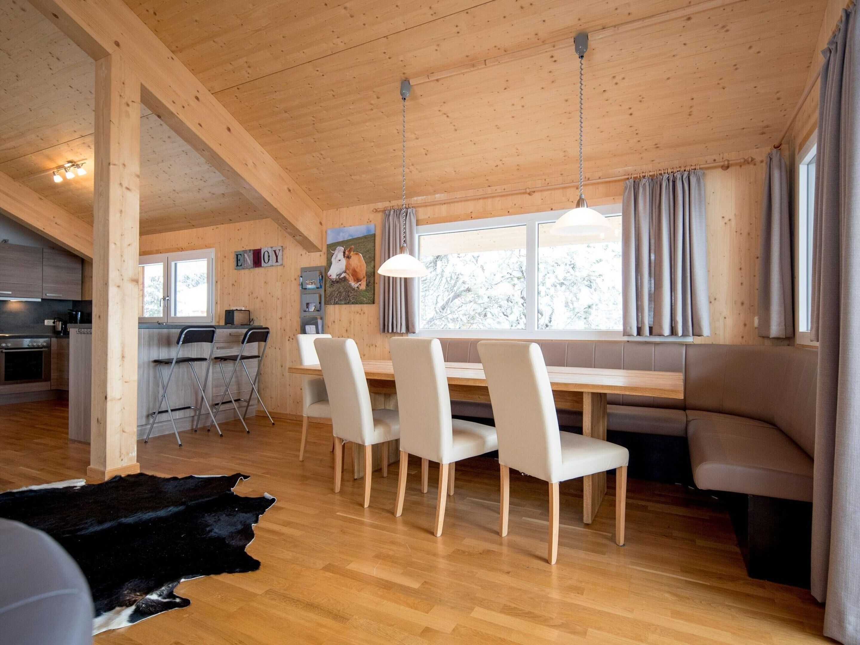 A cozy cabin interior with a wooden dining area, a kitchen, and a seating area by the window.