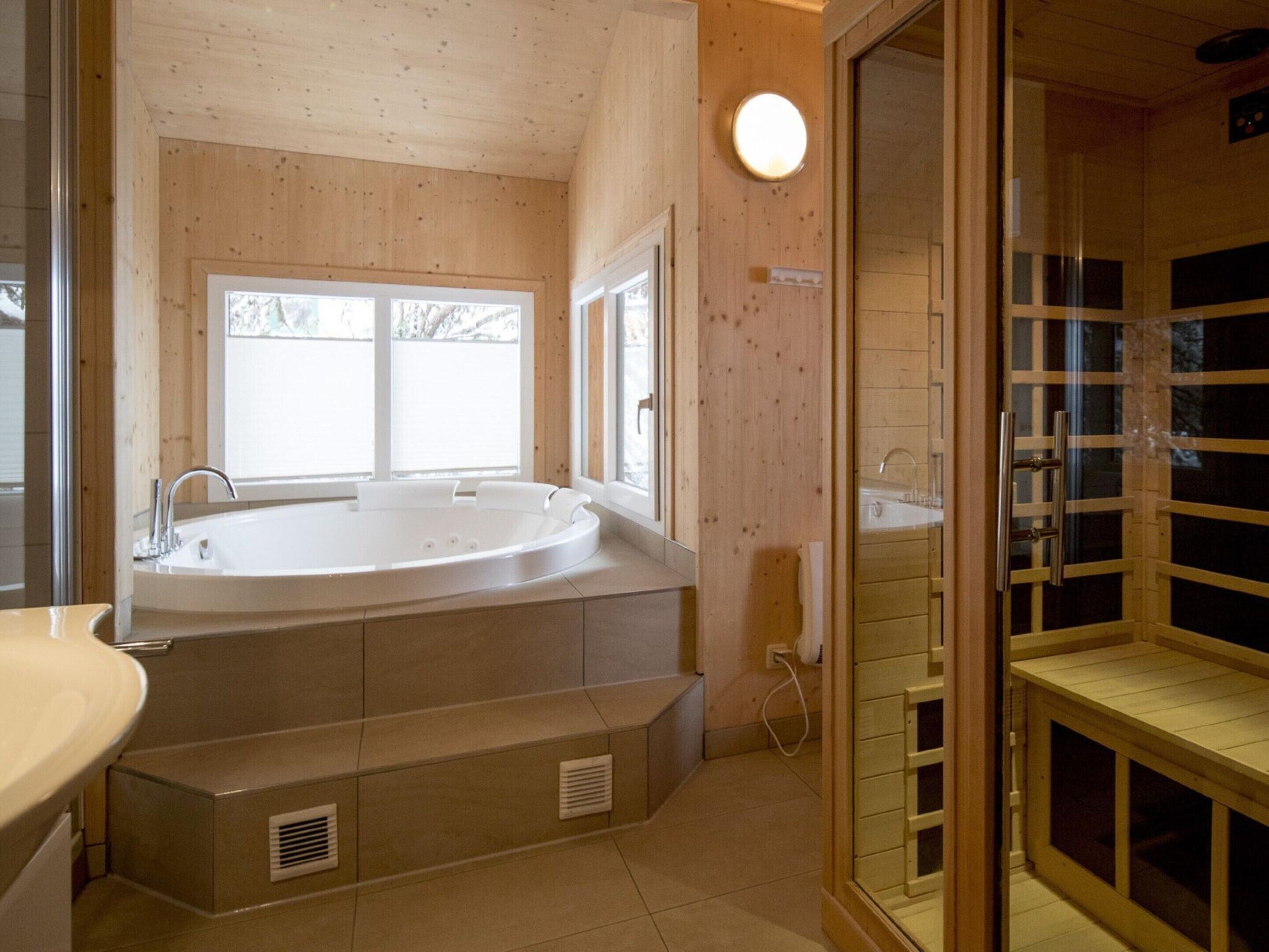 Ein Badezimmer mit einer großen Badewanne, einer Duschkabine und einem Fenster, das für natürliches Licht sorgt.