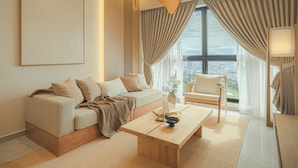 A modern living room with a sofa, armchair, and coffee table, large windows with curtains, and a city view. - NaiBnB @ Agile Bukit Bintang (Kuala Lumpur)