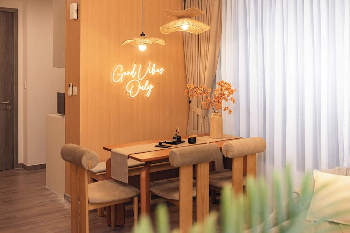 Un comedor moderno con una mesa de madera, sillas acolchadas y un letrero de neón.