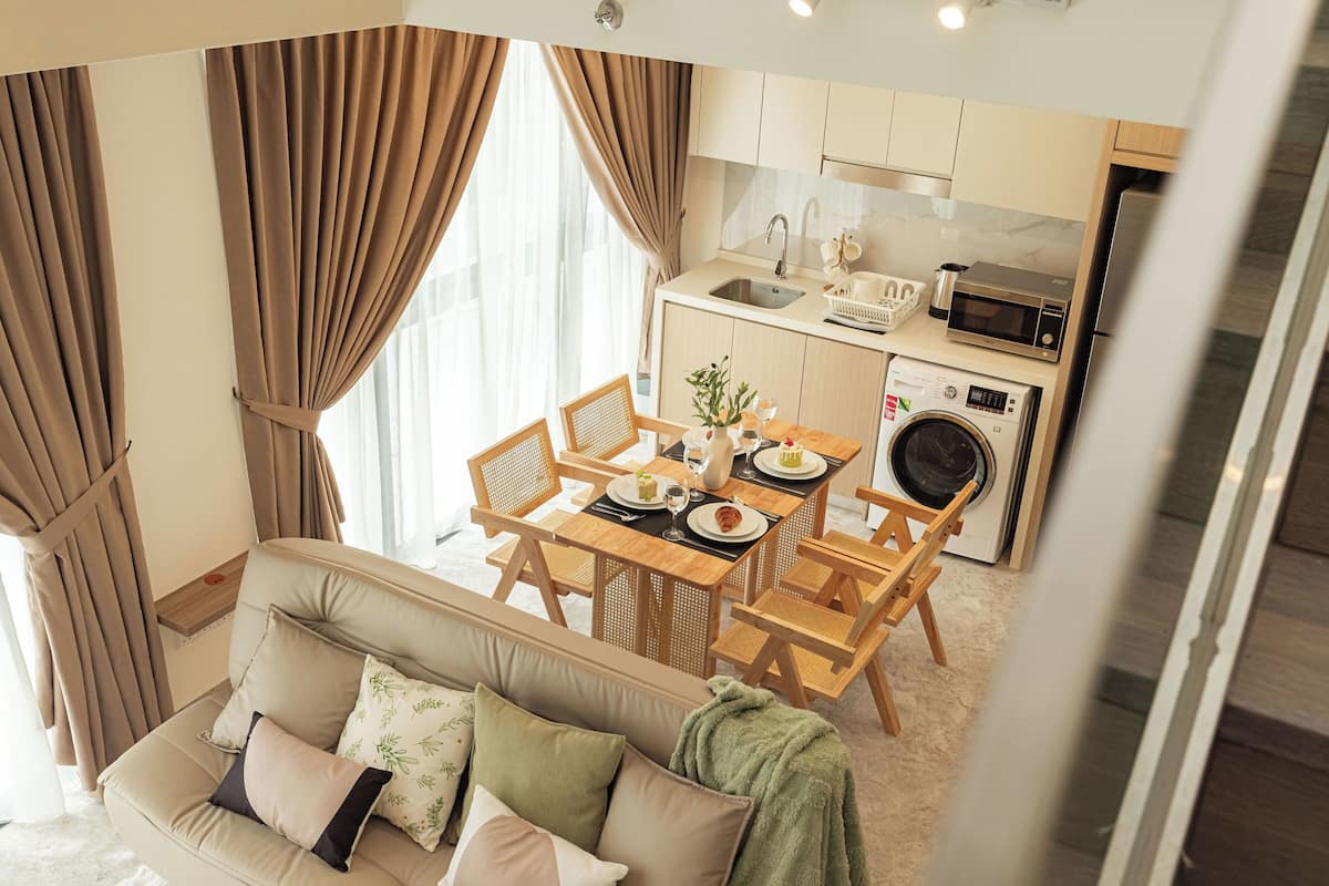 Una sala de estar moderna con sofá, una mesa de comedor y sillas, una cocina equipada y ventanas amplias con cortinas.
