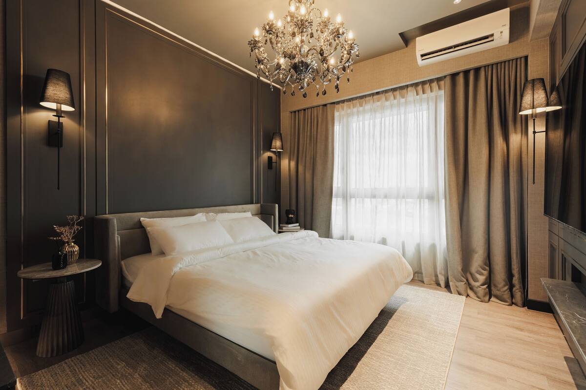 Un dormitorio moderno con una cama grande, una araña, aire acondicionado y vistas al exterior a través de cortinas traslúcidas.