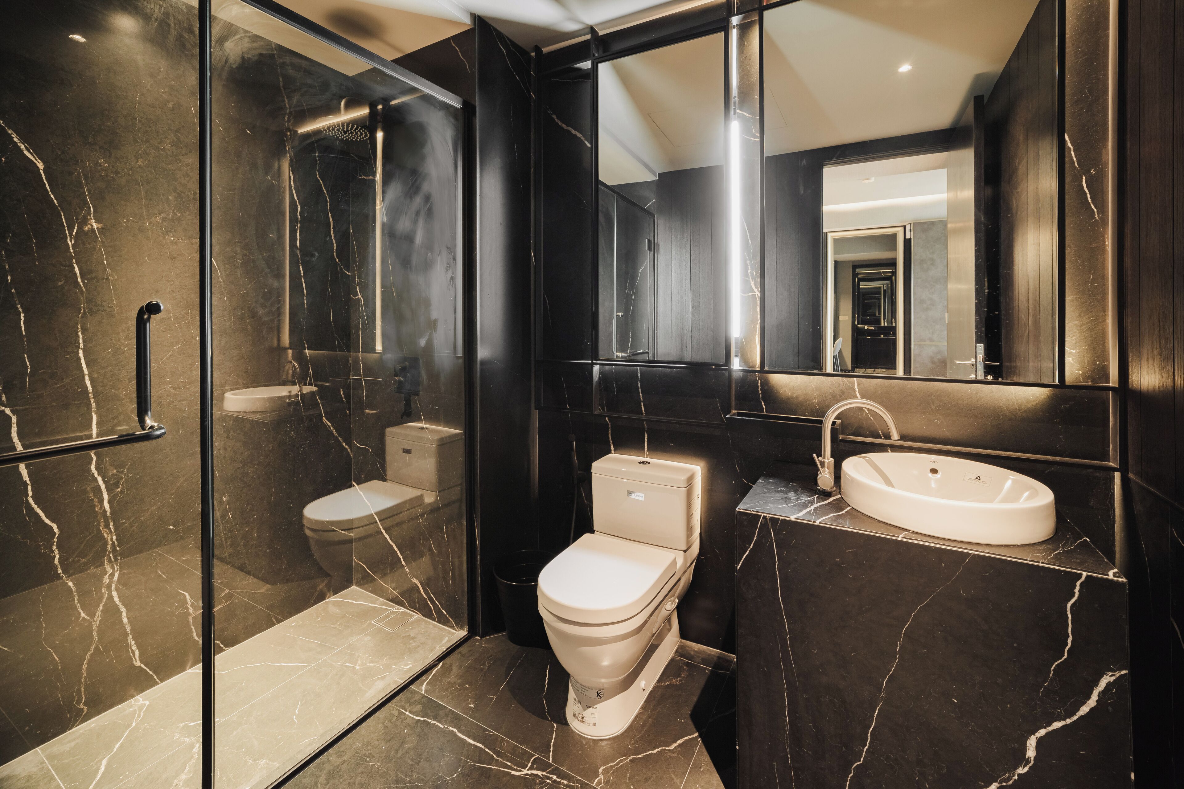 A modern bathroom with a glass-enclosed shower, a toilet, and a sink.
