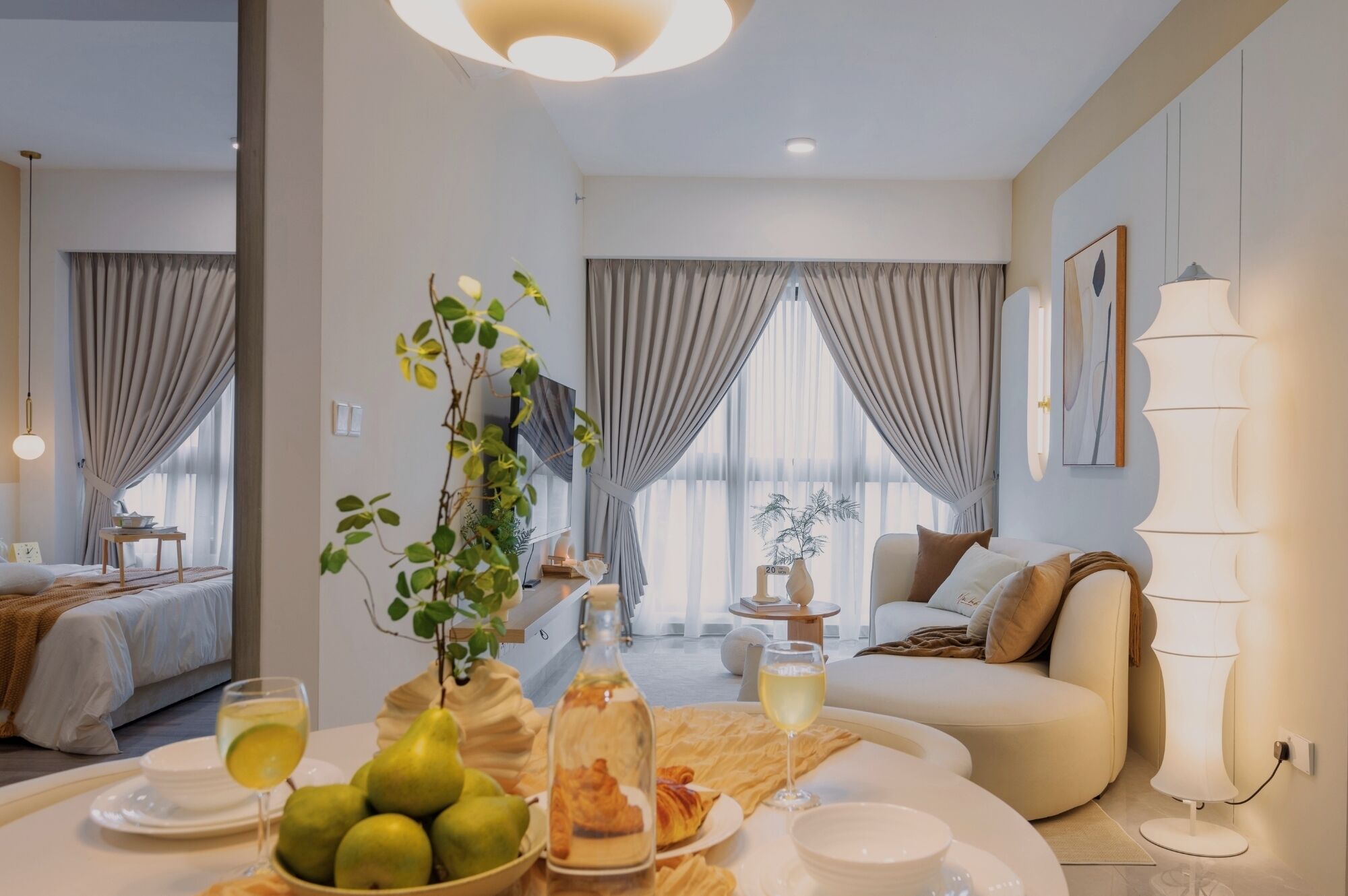 A modern living room with a sofa, a dining table with food and drinks, and a large window with curtains.