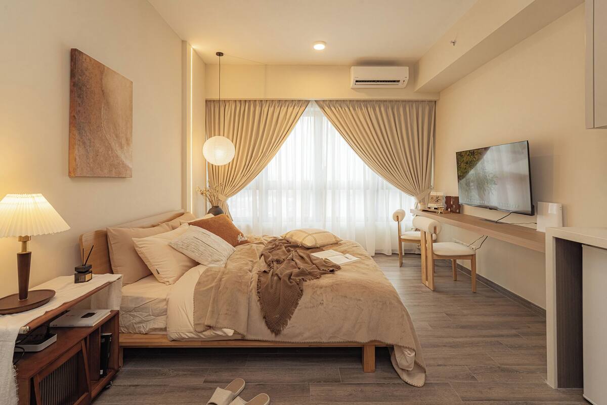 Habitación de hotel con cama, escritorio, televisión y ventana con cortinas.