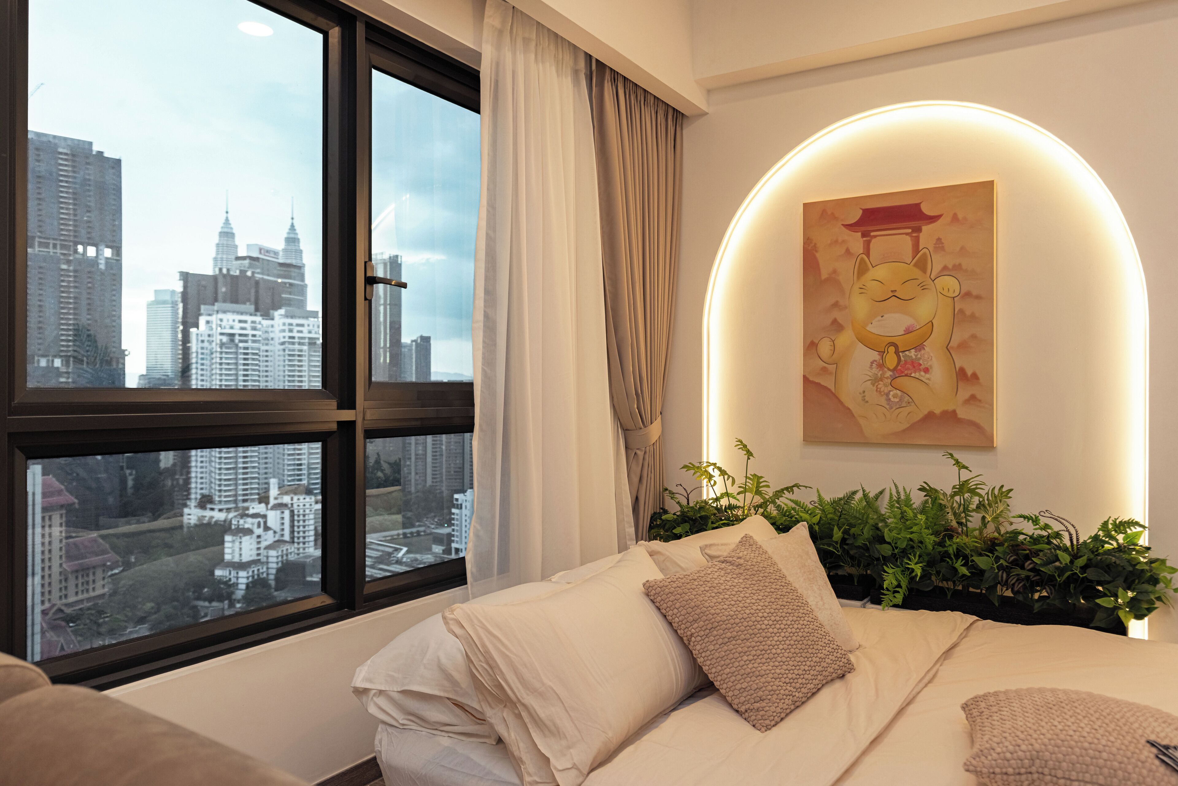 A hotel room with a bed, a city view, a wall-mounted painting, and a plant.