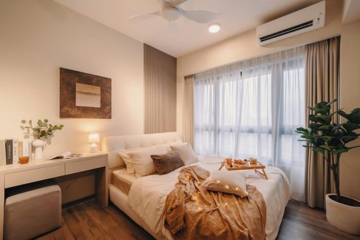 Quarto de hotel com cama, mesa de cabeceira, luminária, planta em vaso e janela com cortinas.