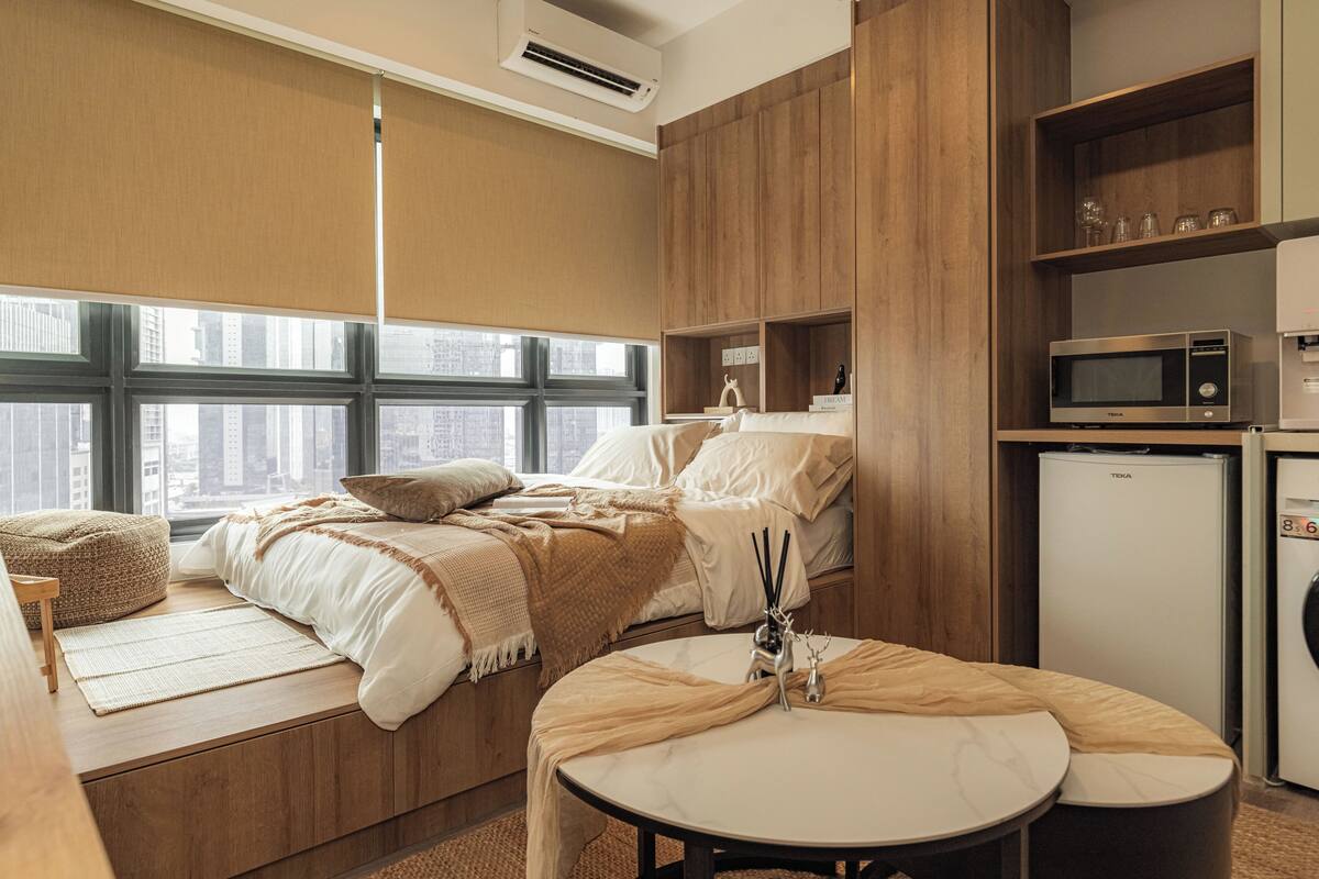 Habitación de hotel compacta con cama, zona de estar, kitchenette y vistas a la ciudad.