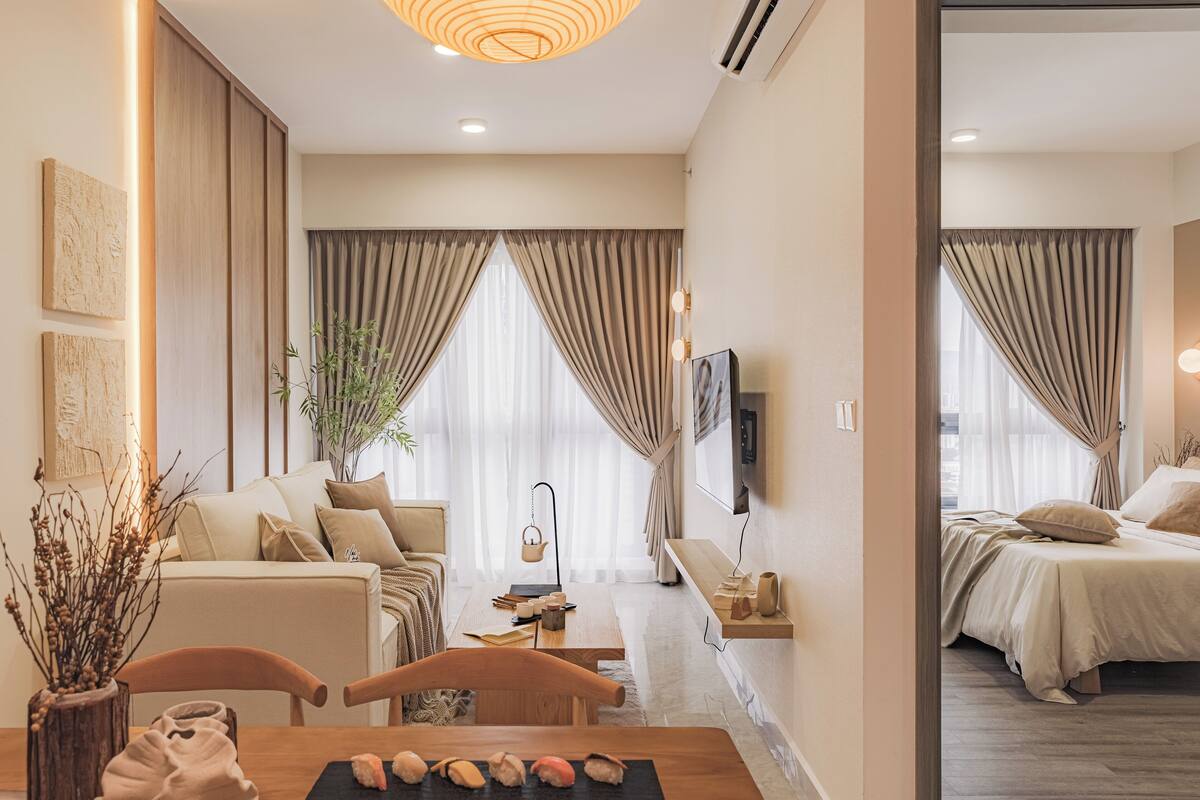 Una habitación de hotel moderna con un sofá, una mesa de comedor con un jarrón de plantas secas y una cama con cabecero.