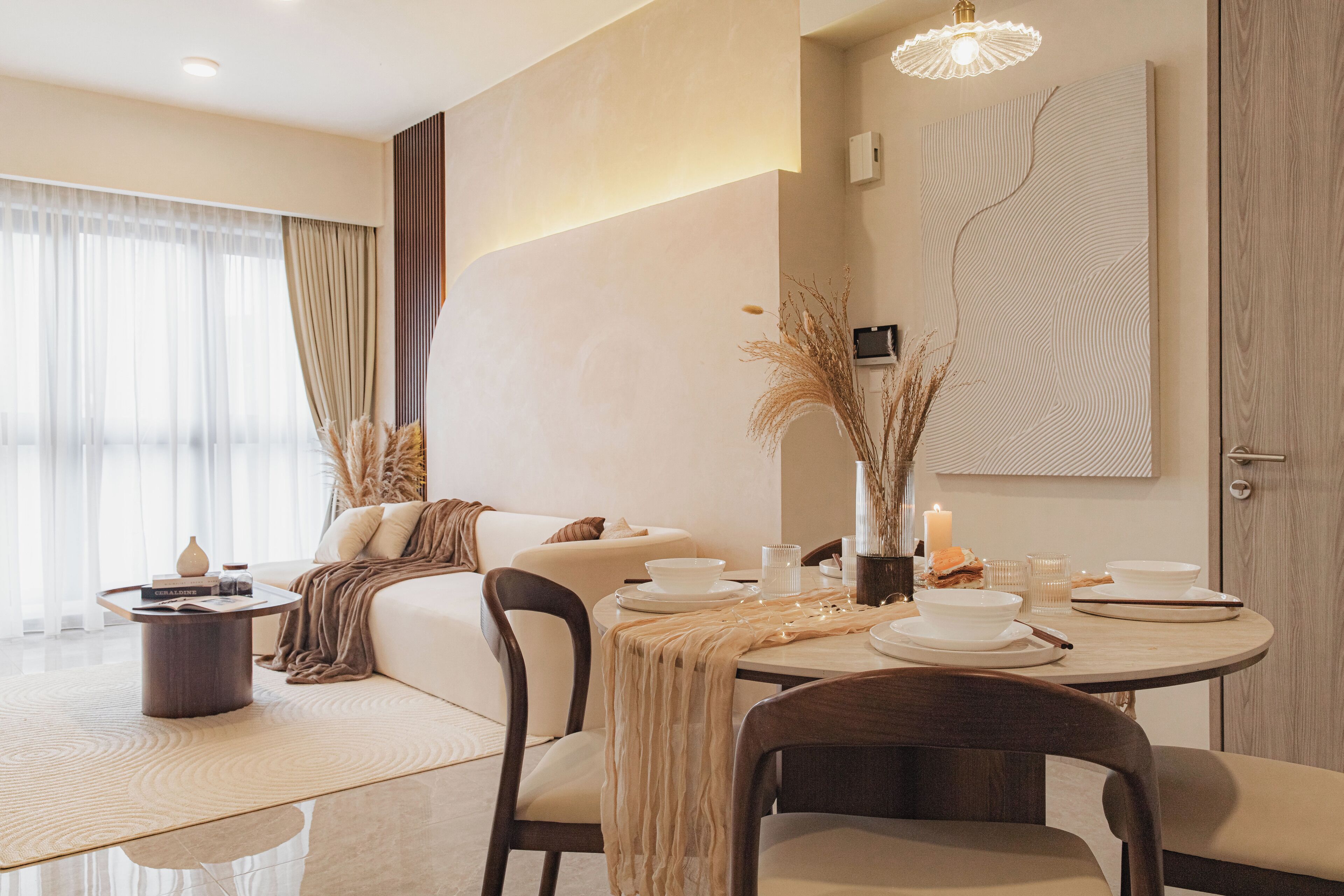 Un comedor moderno con una mesa redonda para dos personas, un sofá y un jarrón decorativo con plumas de pampa.