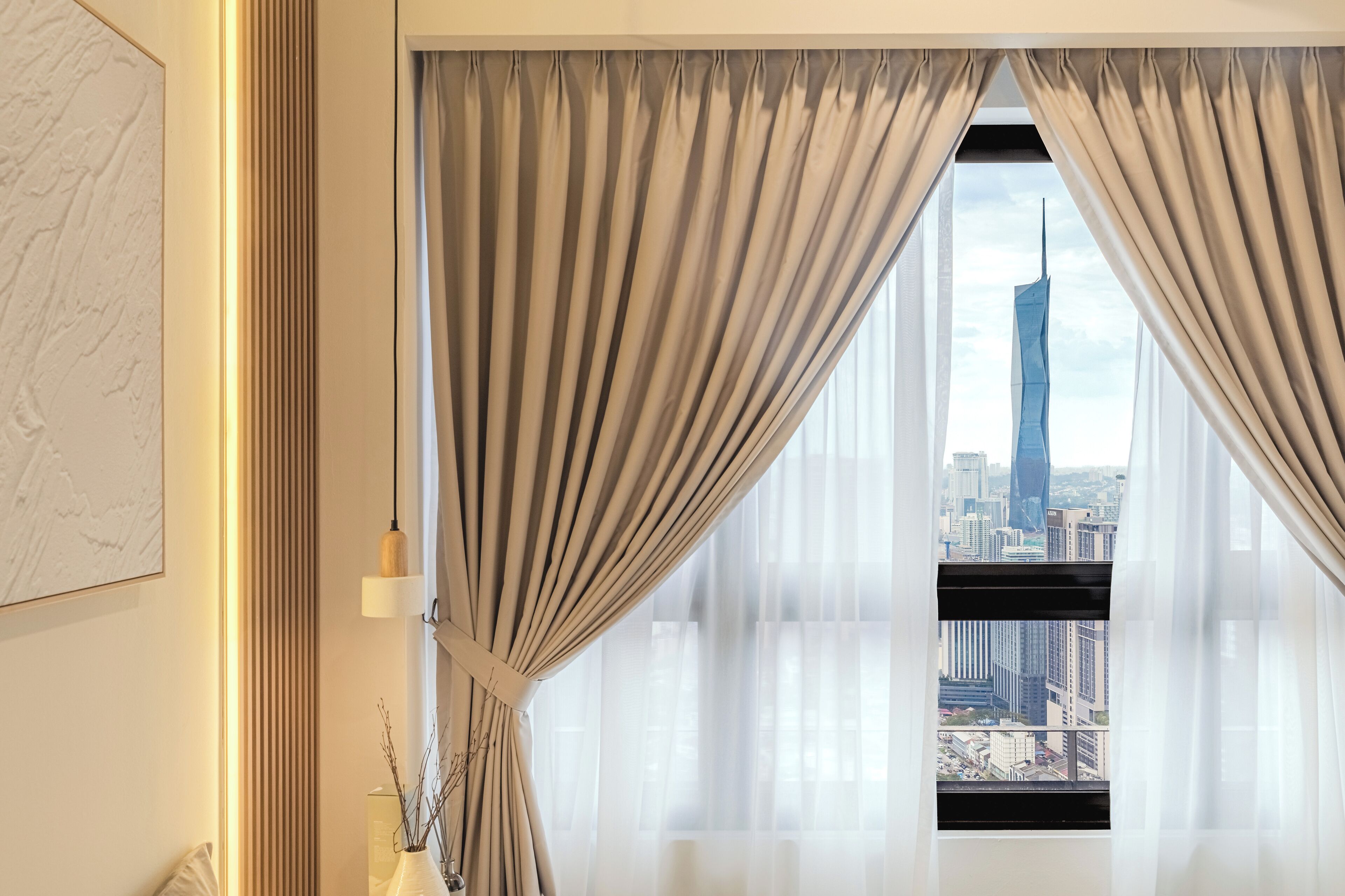 A room with a large window, curtains, a vase with branches, and a cityscape view.