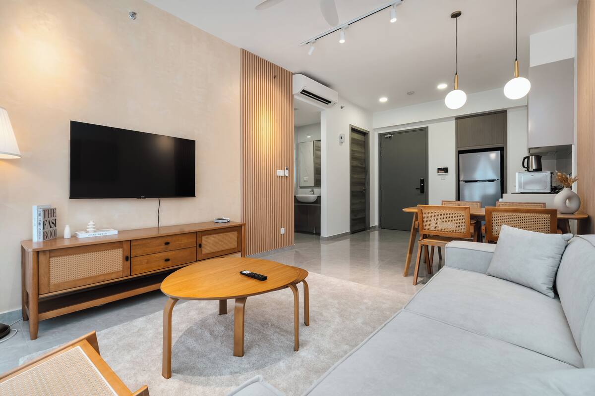 Una sala de estar moderna con un televisor de pantalla plana, muebles de madera, un sofá y un comedor con sillas y una mesa.