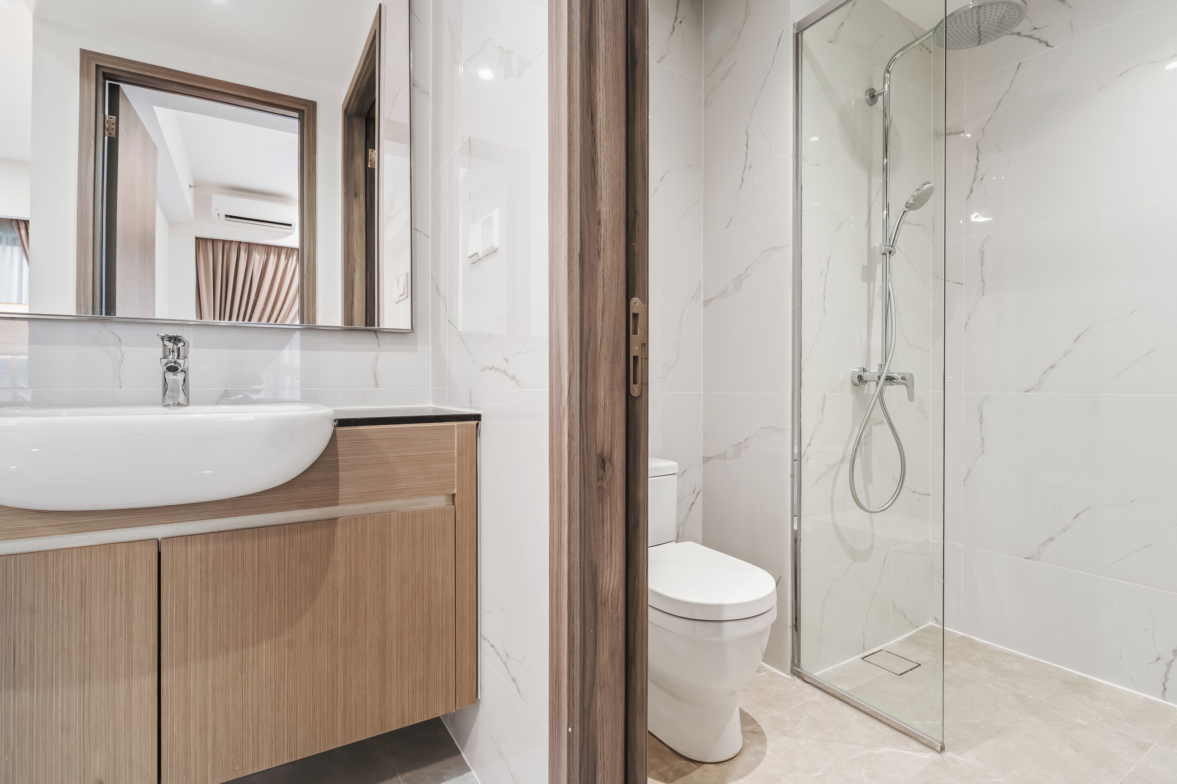 A modern bathroom with a white sink, wooden vanity, a glass shower enclosure, and a toilet.