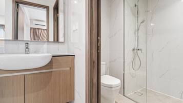Une salle de bain moderne avec un lavabo blanc, un meuble-lavabo en bois, une cabine de douche en verre et des toilettes.