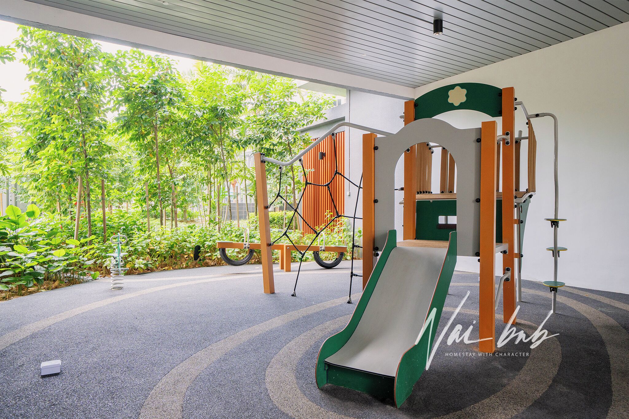 A playground with a slide and climbing structures, surrounded by greenery.