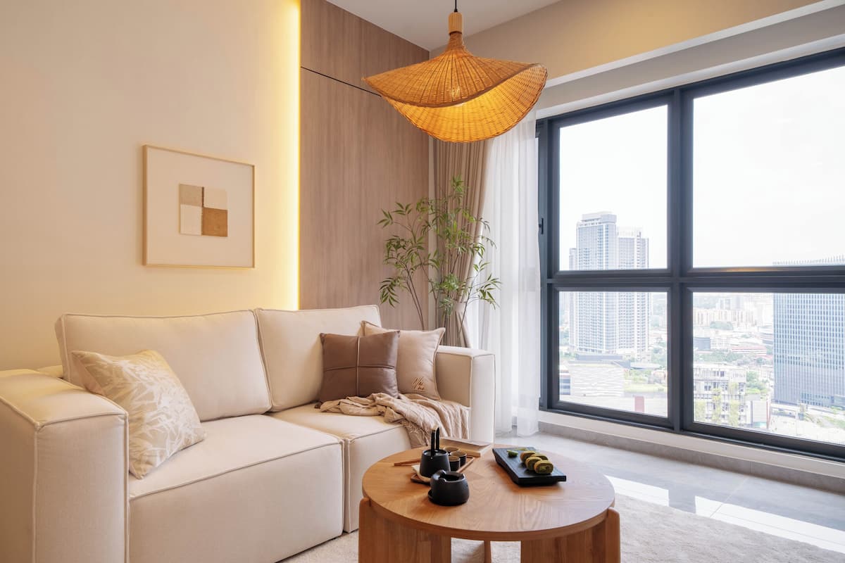 Una sala de estar moderna con un sofá, una mesa de centro redonda de madera, una lámpara colgante y un ventanal con vistas a la ciudad.
